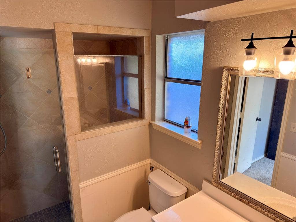 Walk-in shower with tile surround, glass enclosure, opaque window, and dual-bulb wall-mounted vanity lighting