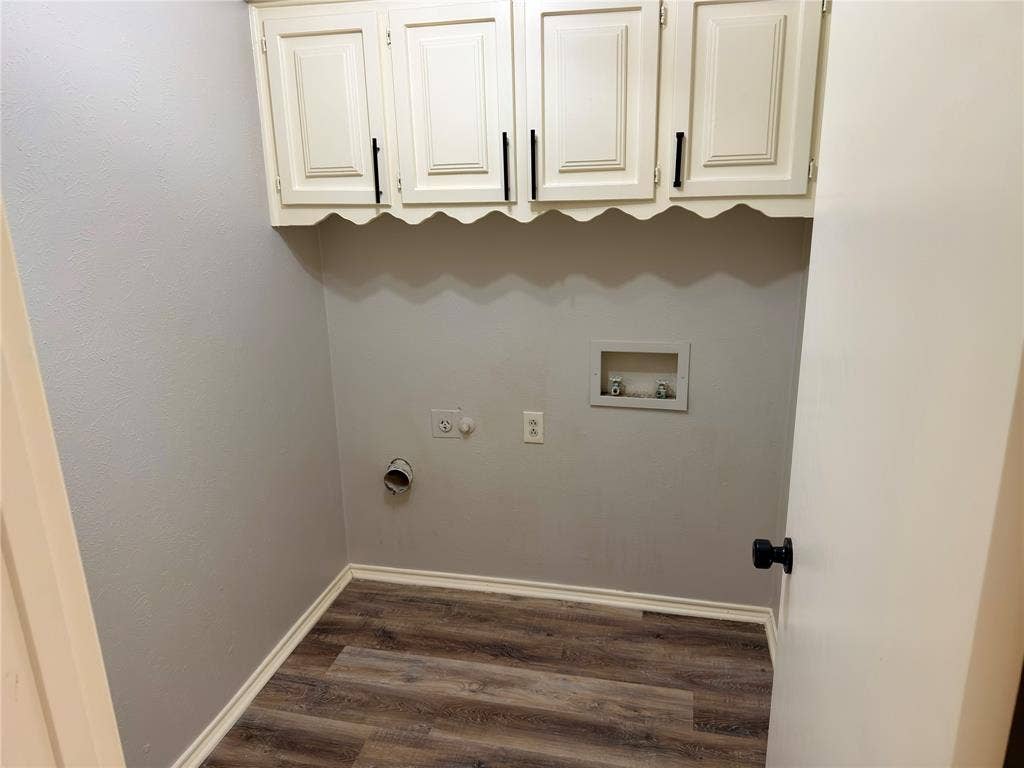 Laundry area featuring wood-finish flooring, white wall-mounted cabinetry with scalloped detailing, and matte black hardware