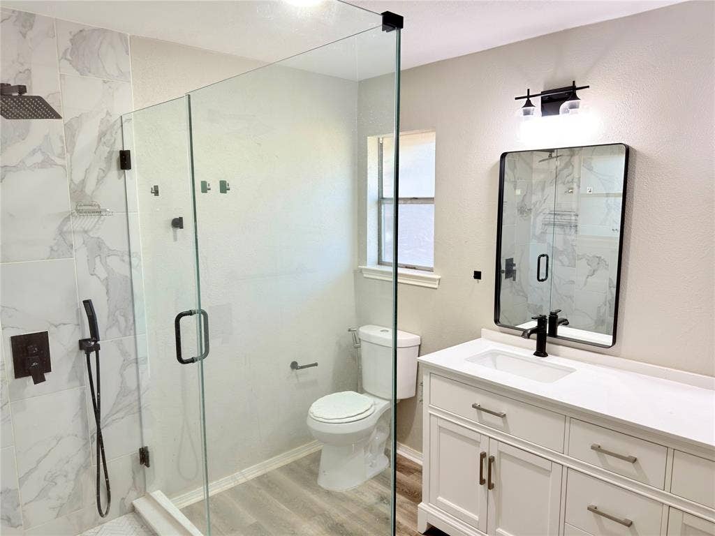Bathroom featuring a frameless glass-enclosed shower with large-format tile surround, rainfall showerhead, and handheld sprayer