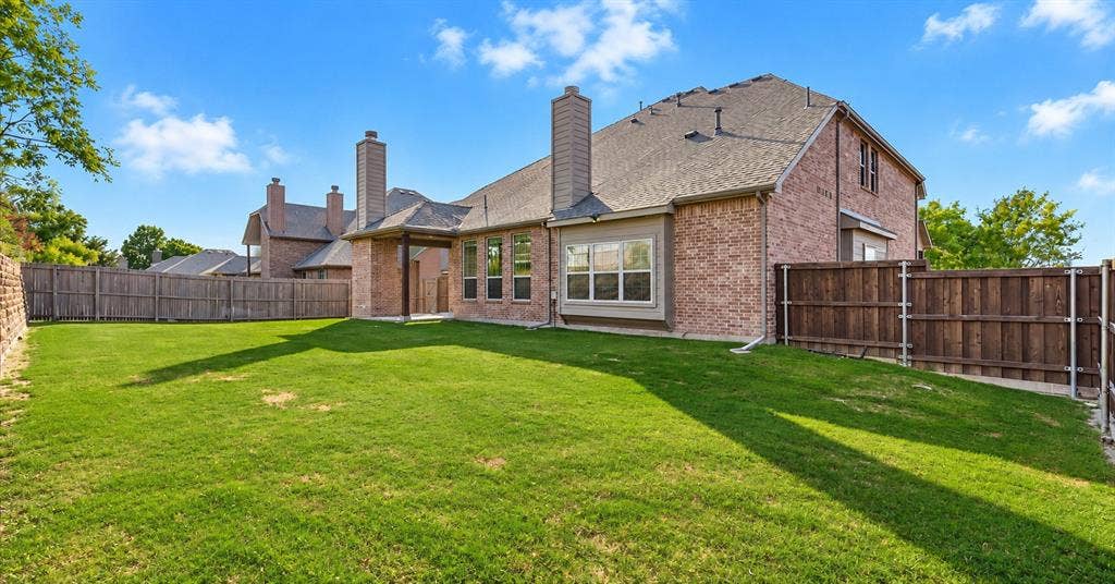 632 Grisham Drive, Fate, TX 75087 Brick exterior with dual masonry chimneys, covered patio, and fenced backyard featuring a manicured lawn