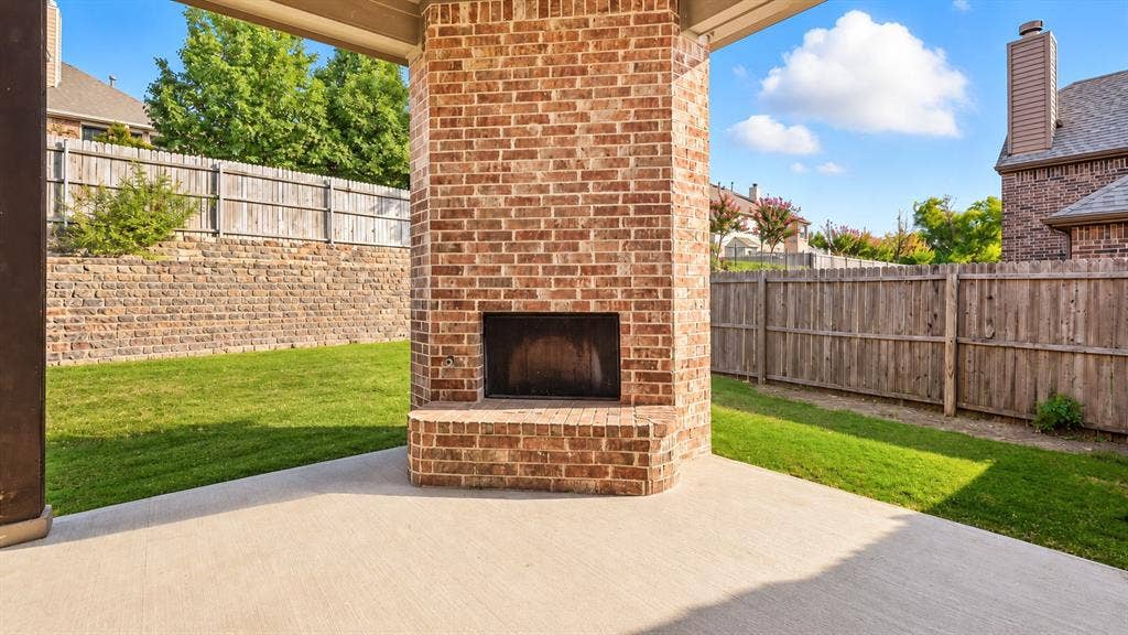 632 Grisham Drive, Fate, TX 75087 Covered patio featuring a floor-to-ceiling brick fireplace with a raised hearth, concrete flooring, and an enclosed backyard with wood fencing