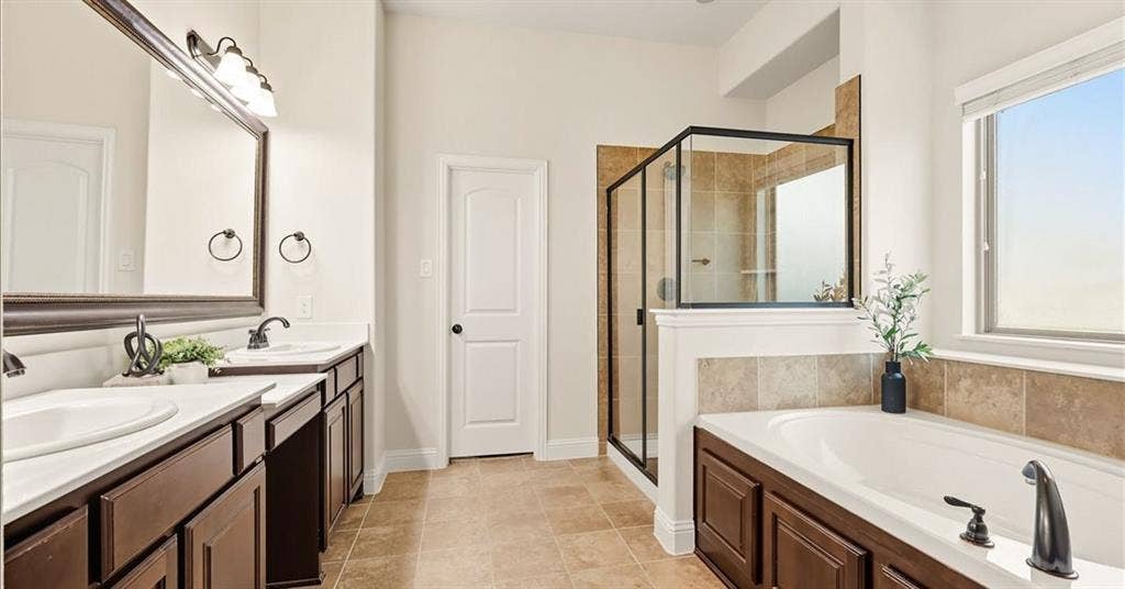 632 Grisham Drive, Fate, TX 75087 Double vanity with dark wood-finish cabinetry, soaking tub with tile surround, glass-enclosed shower, large framed wall mirror, and tile flooring