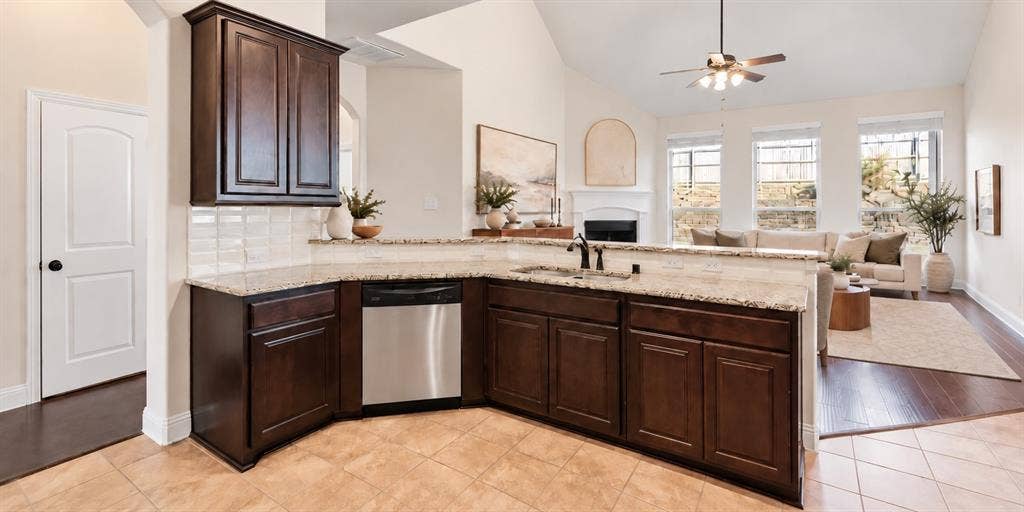 632 Grisham Drive, Fate, TX 75087 Kitchen featuring dark wood cabinetry, stone countertops, stainless steel dishwasher, vaulted ceiling, and fireplace