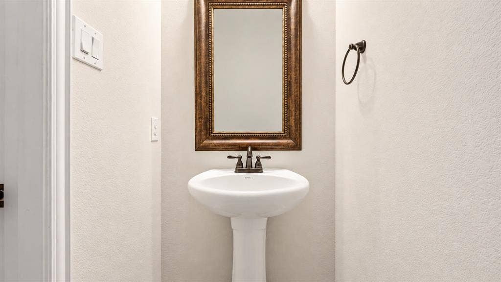 632 Grisham Drive, Fate, TX 75087 White pedestal sink with a dual-handle bronze faucet, complemented by a framed rectangular mirror and a matching bronze towel ring