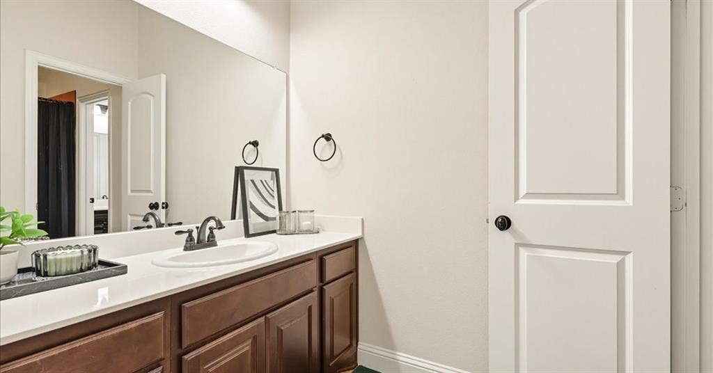 632 Grisham Drive, Fate, TX 75087 Bathroom featuring dark wood cabinetry, a light-toned countertop with an integrated basin, a widespread faucet, a large vanity mirror, and a two-panel interior door