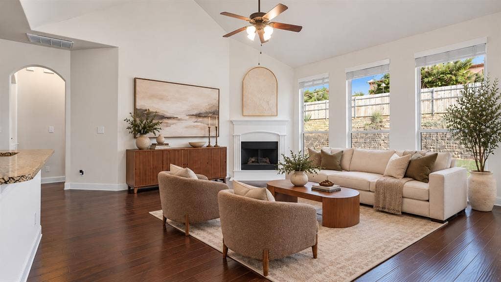 632 Grisham Drive, Fate, TX 75087 Living area featuring vaulted ceilings, wood-finish flooring, corner fireplace with a white mantel, and large windows