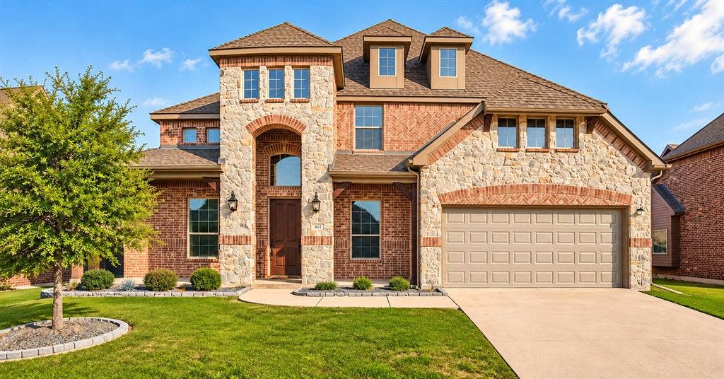 632 Grisham Drive, Fate, TX 75087 Two-story exterior featuring a brick and stone facade, arched entryway, dormer windows, and a multi-car garage