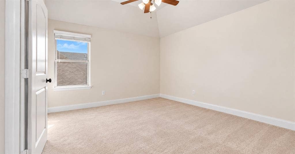 632 Grisham Drive, Fate, TX 75087 Neutral-toned room featuring a vaulted ceiling, textured carpet, single-pane window, and a central ceiling fan with integrated light fixture