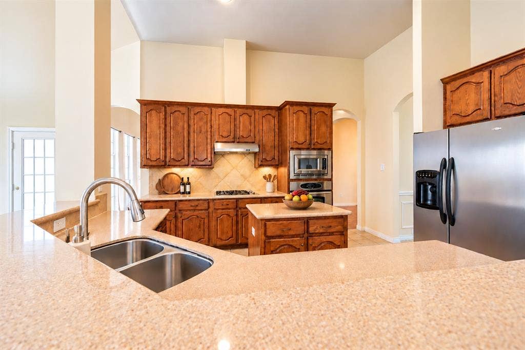 1736 Blue Stream Drive, DeSoto, TX 75115 Kitchen featuring wood cabinetry, granite countertops, stainless steel appliances, a center island, and a double-basin undermount sink *Virtually staged to show potential*