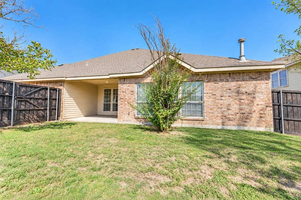 1736 Blue Stream Drive, DeSoto, TX 75115 Rear exterior featuring a brick facade, covered concrete patio, asphalt shingle roof, and wooden privacy fencing