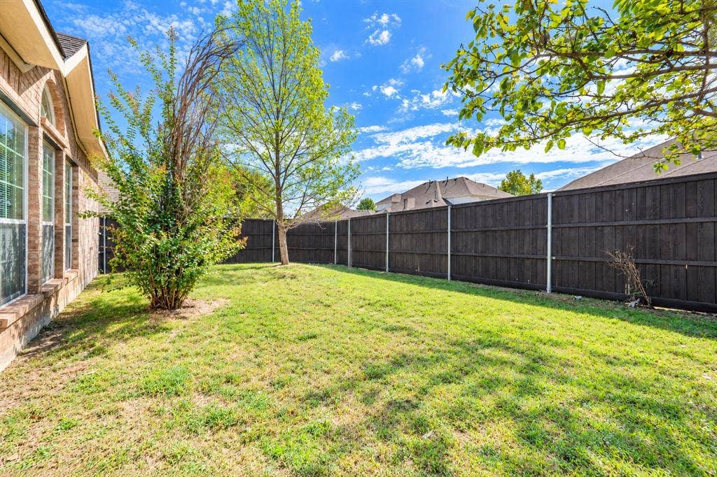 1736 Blue Stream Drive, DeSoto, TX 75115 Rear exterior featuring a brick facade, manicured lawn, and full-height wood fencing
