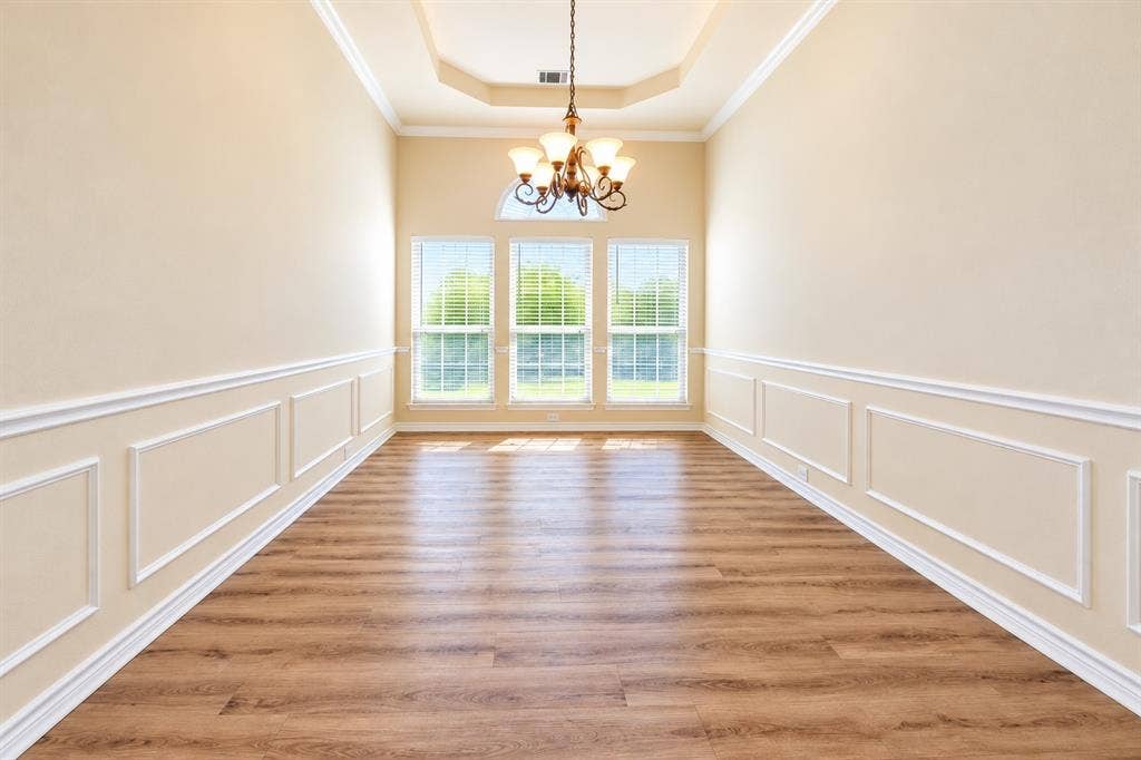 1736 Blue Stream Drive, DeSoto, TX 75115 Formal dining room featuring wood-look LVP flooring, wainscoting, a tray ceiling, an arched window, and a multi-arm chandelier