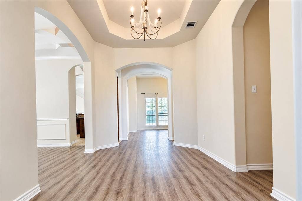 1736 Blue Stream Drive, DeSoto, TX 75115 Foyer featuring wood-look LVP flooring, a tray ceiling, an integrated chandelier, and prominent arched architectural openings