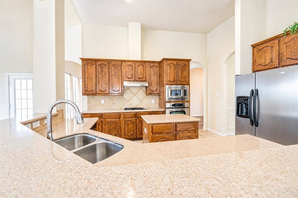 1736 Blue Stream Drive, DeSoto, TX 75115 Kitchen featuring high-vaulted ceilings, granite countertops, stained wood cabinetry, stainless steel appliances, and a central island