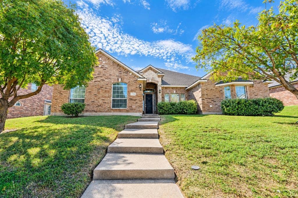 1736 Blue Stream Drive, DeSoto, TX 75115 Brick exterior with multi-gabled roofline, arched entryway, concrete stairs, and mature landscaping