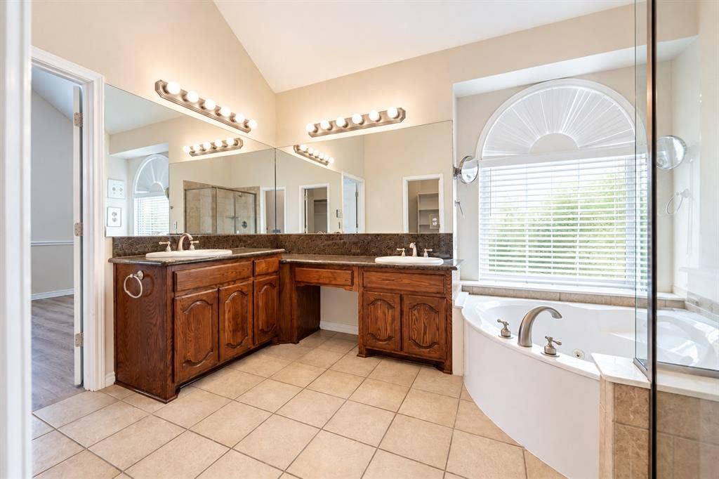 1736 Blue Stream Drive, DeSoto, TX 75115 Dual-sink vanity with stone countertop, tile flooring, corner soaking tub, and arched window with integrated shutters
