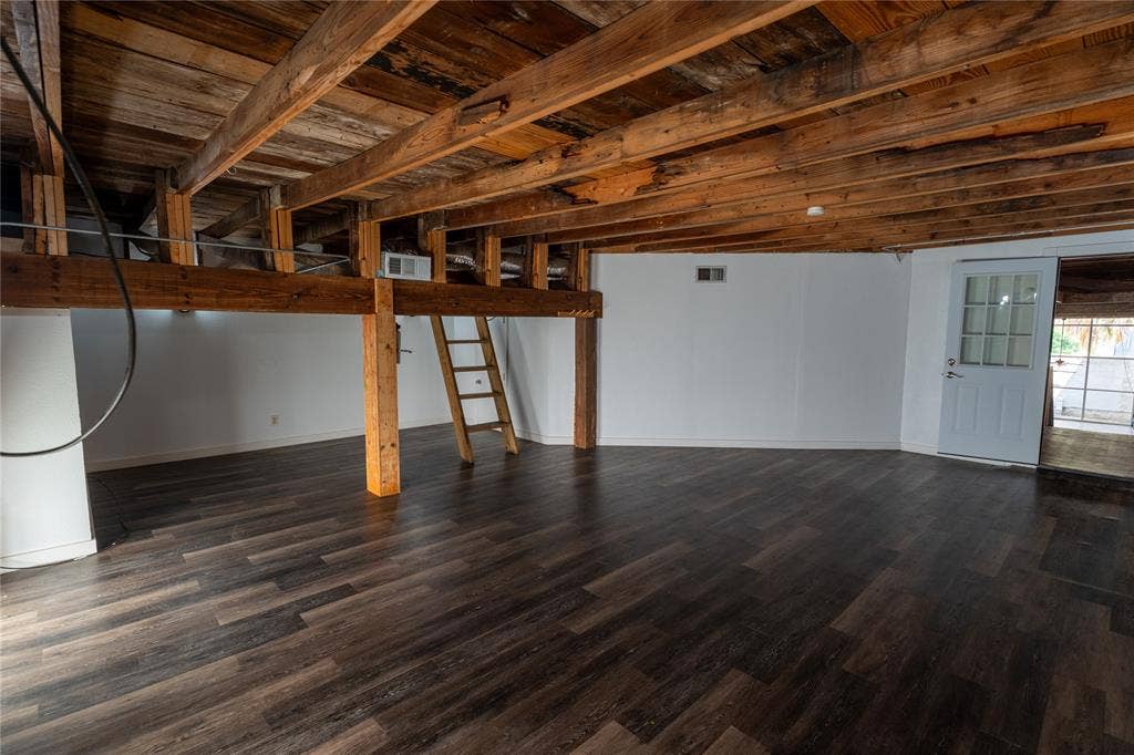 3014 Canton Street, Dallas, TX 75226 Interior space featuring exposed wooden ceiling beams and support posts, wood-finish flooring, white walls, and a multi-pane glass-panel door