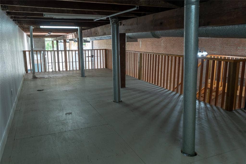 3014 Canton Street, Dallas, TX 75226 Industrial-style loft space featuring exposed timber beam ceiling, raw brick wall, metallic support columns, and wooden balustrades