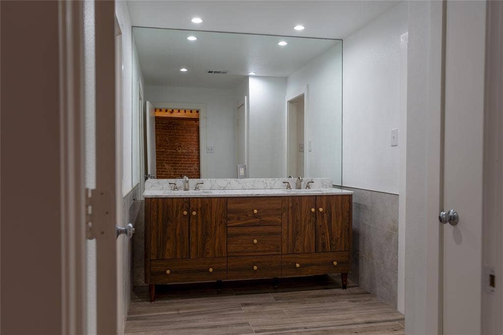 3014 Canton Street, Dallas, TX 75226 Dual-sink vanity with wood-finish cabinetry, stone countertop, integrated lighting, and full-width wall mirror over tile wainscoting