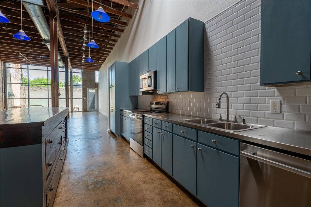 3014 Canton Street, Dallas, TX 75226 Exposed timber ceiling beams, polished concrete flooring, stainless steel appliances, blue-toned cabinetry, and white subway tile backsplash