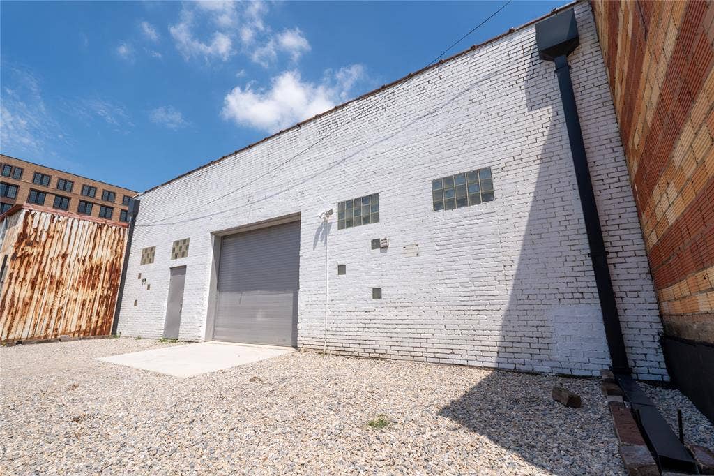3014 Canton Street, Dallas, TX 75226 Painted brick exterior featuring a roll-up loading door, pedestrian door, glass block windows, and an external drainage downspout