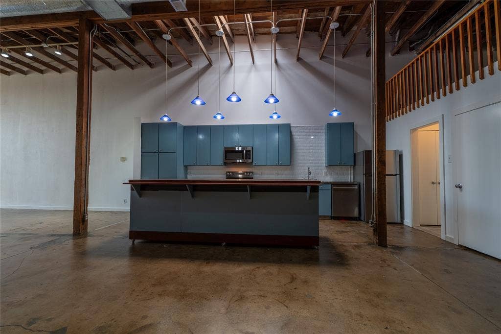 3014 Canton Street, Dallas, TX 75226 Open-concept kitchen featuring exposed wood beam ceilings, polished concrete flooring, blue cabinetry, a wood-topped island, and a mezzanine level with a wooden railing