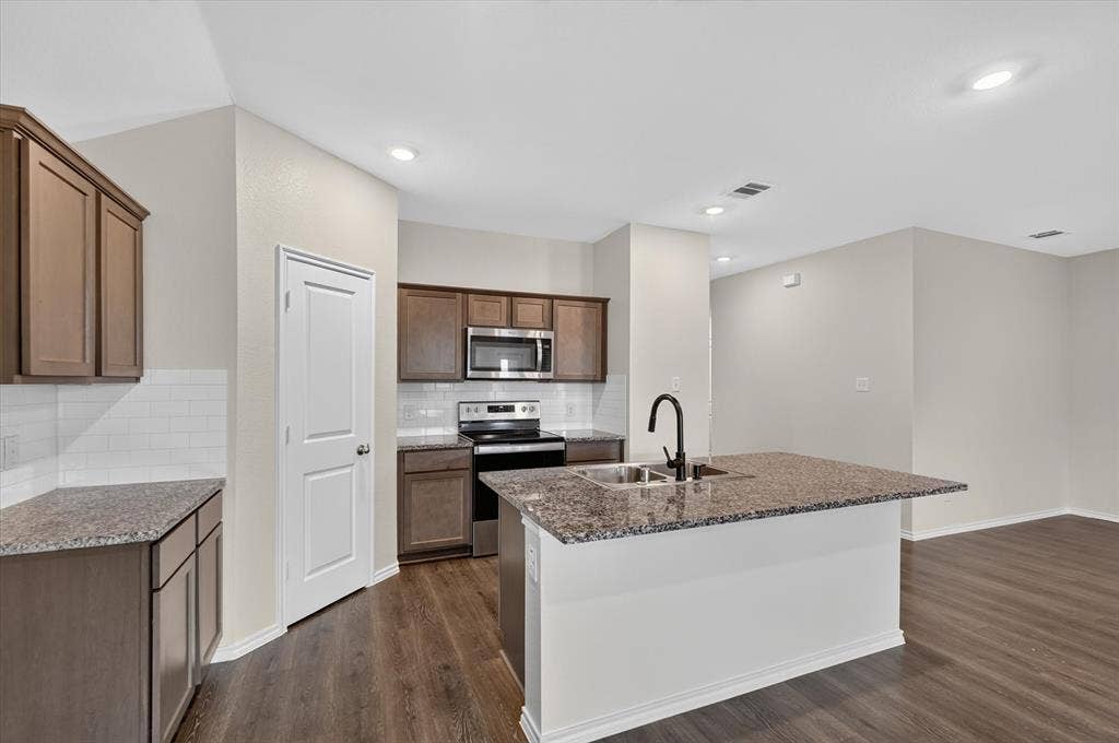 114 Real Quiet Lane, Caddo Mills, TX 75135 Kitchen featuring stone-finish countertops, shaker-style cabinetry, white subway tile backsplash, a center island with a matte black faucet, and wood-finish flooring