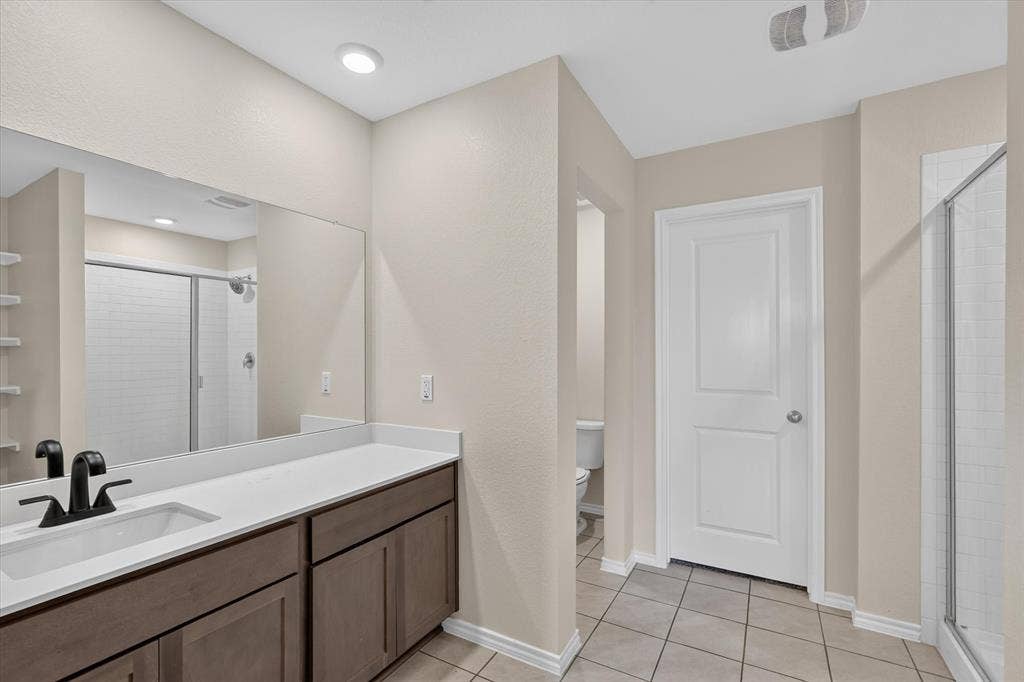 114 Real Quiet Lane, Caddo Mills, TX 75135 Bathroom featuring a vanity with dark-finish cabinetry, a white countertop, and a matte black faucet, complemented by a large wall-mounted mirror, ceramic tile flooring, and a glass-enclosed shower