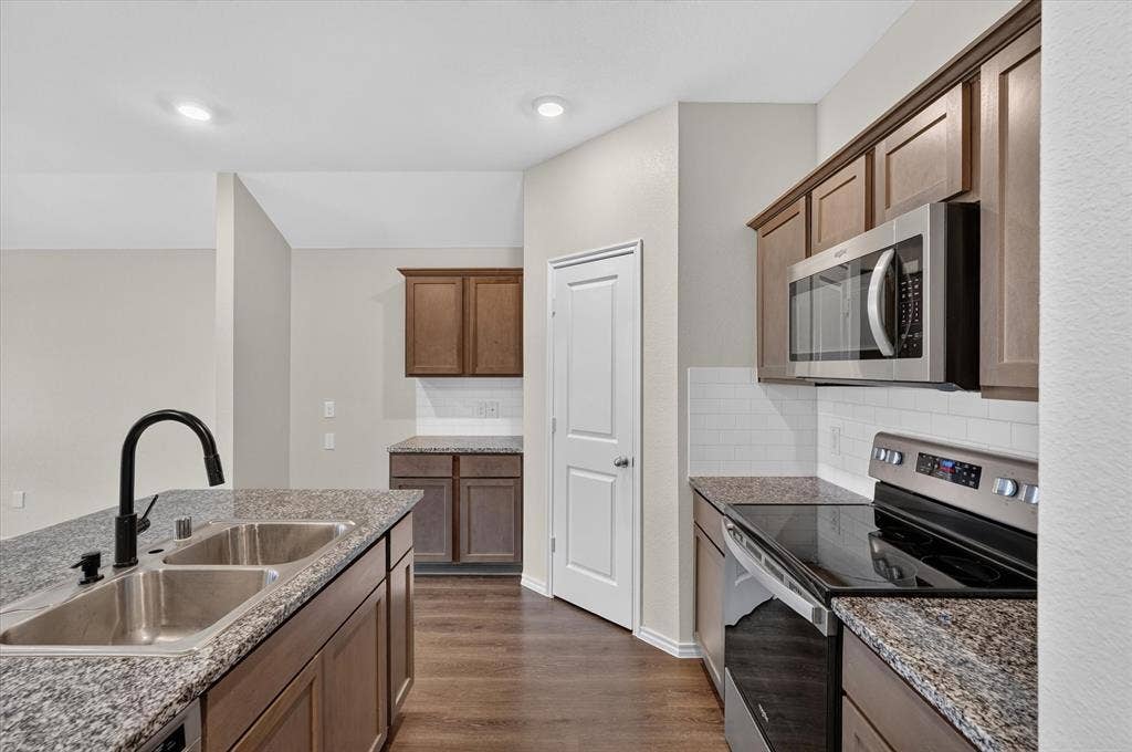 114 Real Quiet Lane, Caddo Mills, TX 75135 Kitchen featuring stone countertops, wood-finish cabinetry, stainless steel appliances, a subway tile backsplash, and a double-basin undermount sink with a matte black faucet