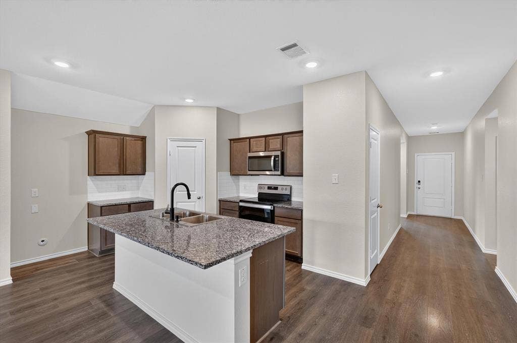 114 Real Quiet Lane, Caddo Mills, TX 75135 Kitchen featuring a stone-topped island with an integrated double-basin sink and matte black faucet, dark wood-finish cabinetry, and wood-finish flooring