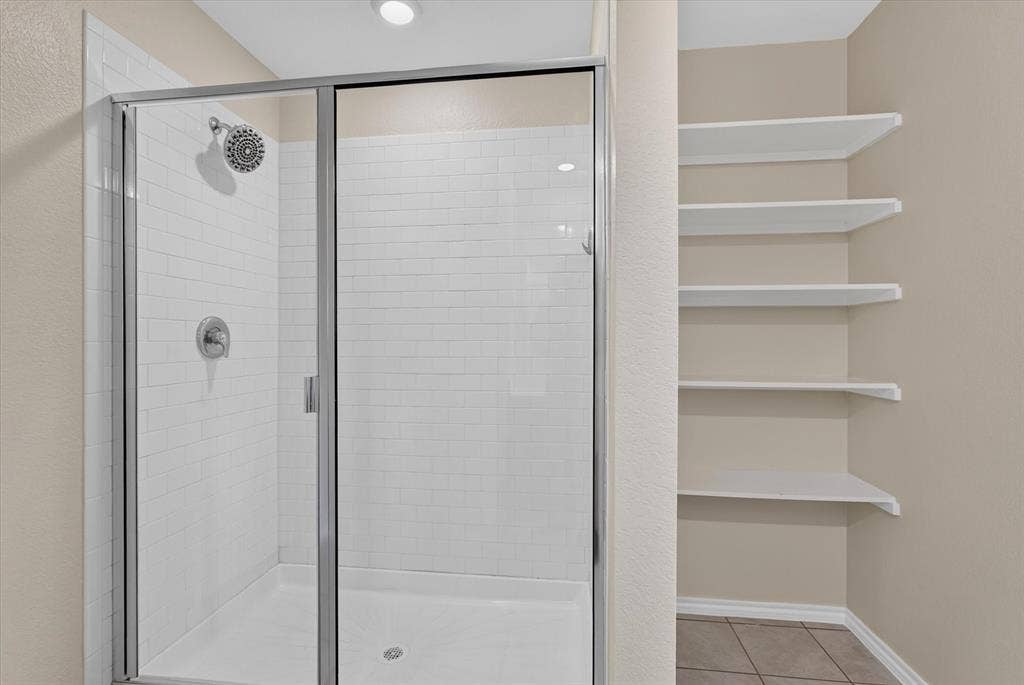 114 Real Quiet Lane, Caddo Mills, TX 75135 Shower enclosure featuring white subway tile walls, a chrome fixture, and a glass sliding door, complemented by built-in white shelving