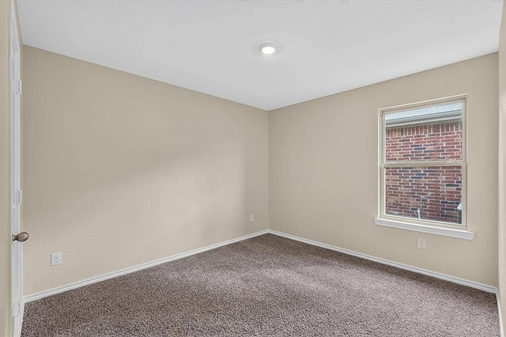 114 Real Quiet Lane, Caddo Mills, TX 75135 Neutral interior room featuring neutral wall paint, carpeted flooring, a flush-mount ceiling light fixture, and a window with a brick exterior backdrop