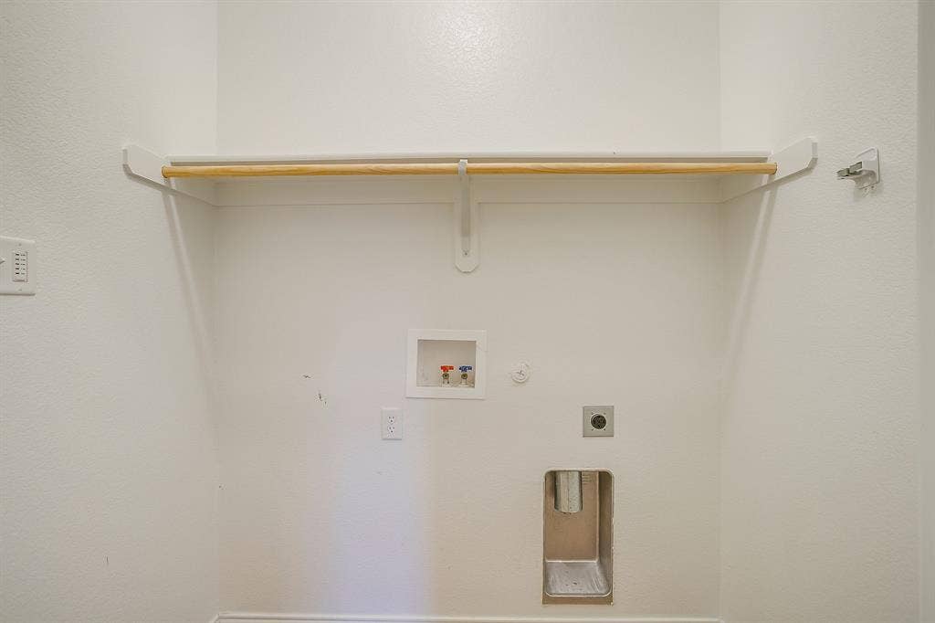 Utility alcove featuring a recessed plumbing connection box, metal dryer vent, and a mounted shelf with a wooden hanging rod