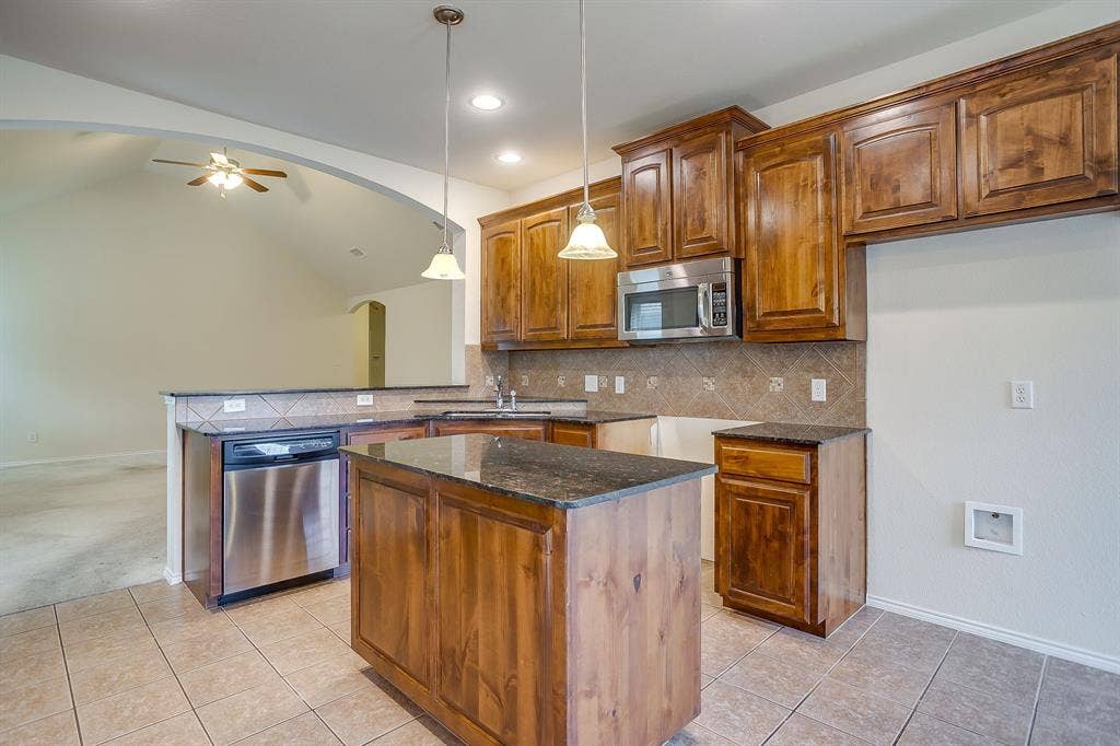 Kitchen featuring wood cabinetry, stone countertops, stainless steel appliances, a center island, and ceramic tile flooring