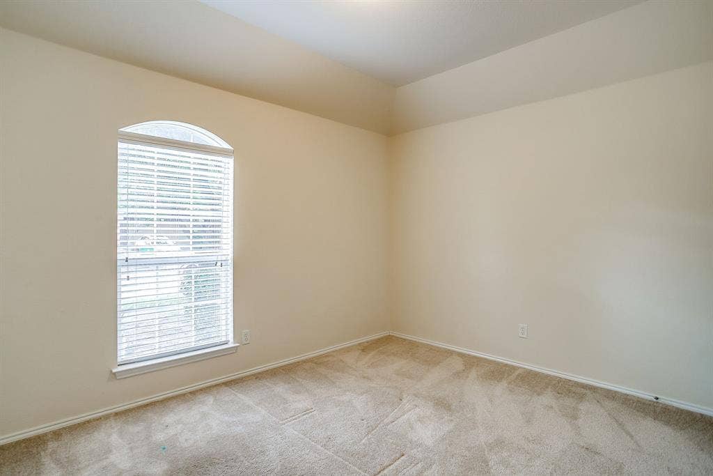 Room with vaulted ceiling, neutral wall tones, wall-to-wall carpeting, and an arched window featuring horizontal blinds