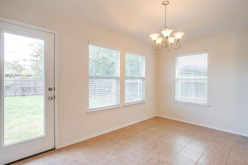 Neutral-toned tile flooring, three large windows with integrated blinds, and an exterior door with glass insert, complemented by a multi-arm metallic chandelier
