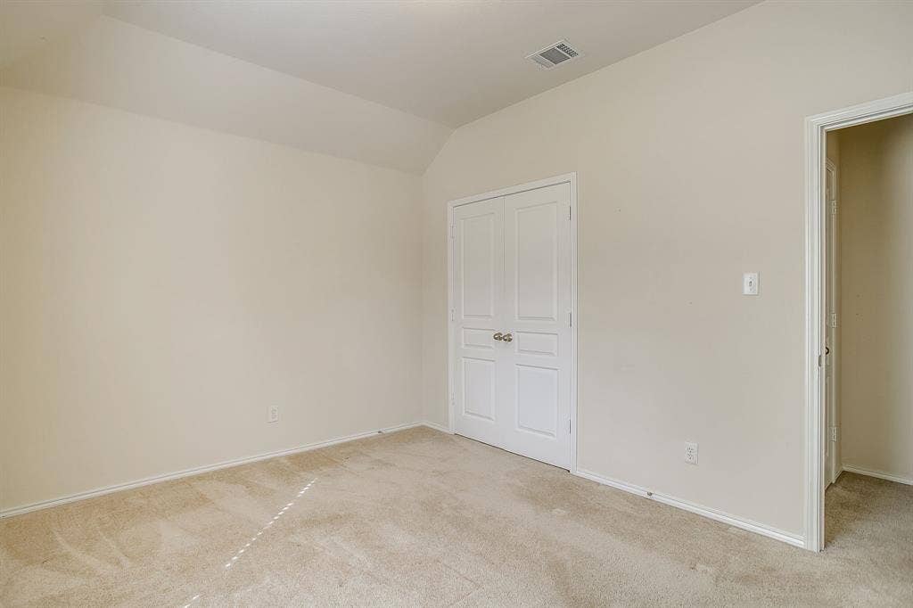 Neutral-toned room featuring vaulted ceilings, carpeting, and double-panel closet doors