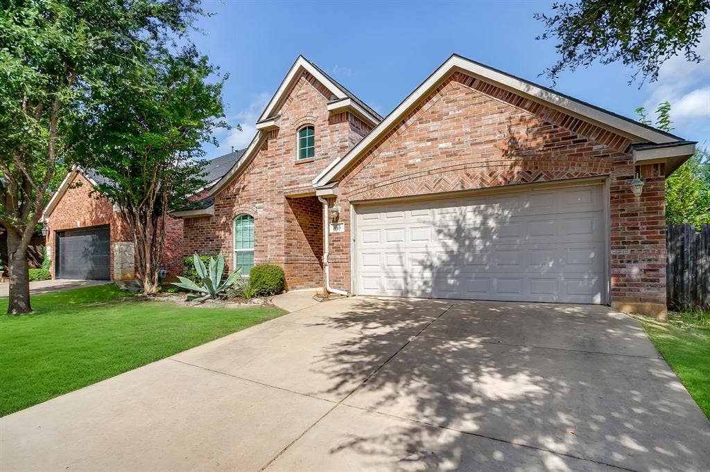 Brick exterior featuring a gabled roofline, arched window detailing, a multi-car garage, and concrete driveway
