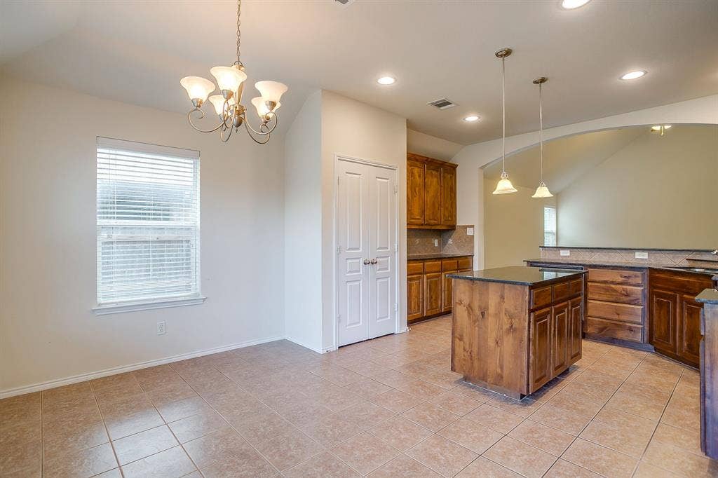 Kitchen featuring natural wood cabinetry, stone countertops, central island, dual hanging pendant lights, and decorative chandelier