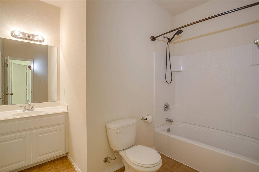 Bathroom featuring a white vanity with a integrated countertop basin, wall-mounted mirror, three-light vanity fixture, and a tub-shower combination with a hand-held showerhead