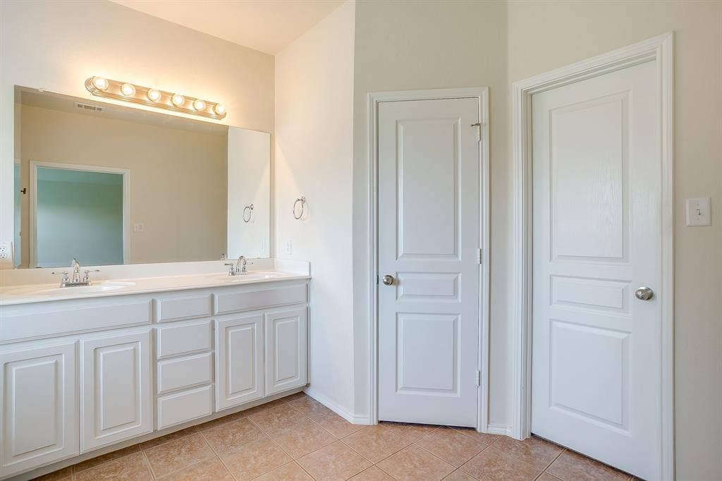 Double vanity with white cabinetry, integrated sinks, large wall-to-wall mirror, six-light fixture, and ceramic tile flooring