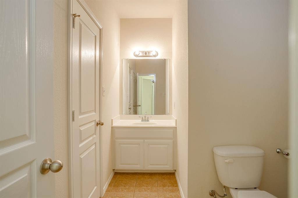 White vanity cabinet featuring a solid-surface countertop with an integrated basin, wall-mounted mirror, two-light fixture, and ceramic tile flooring