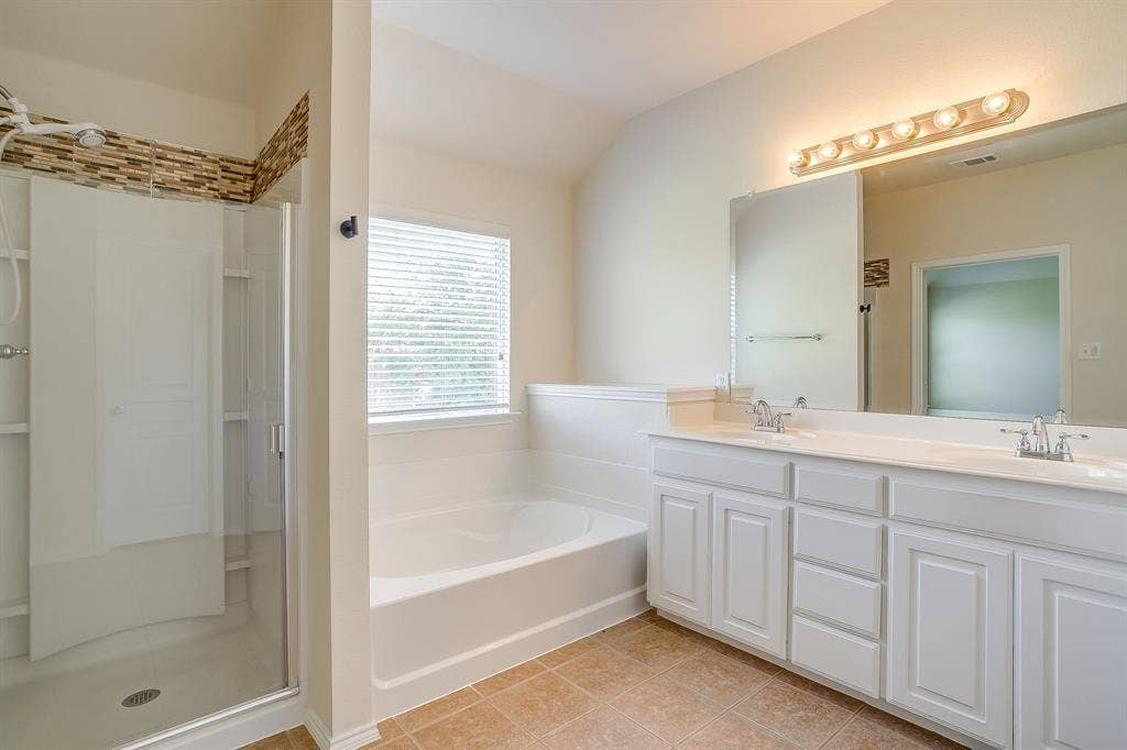 Dual-sink vanity with white cabinetry and a solid-surface countertop, built-in soaking tub, and glass-enclosed shower with tiled accents