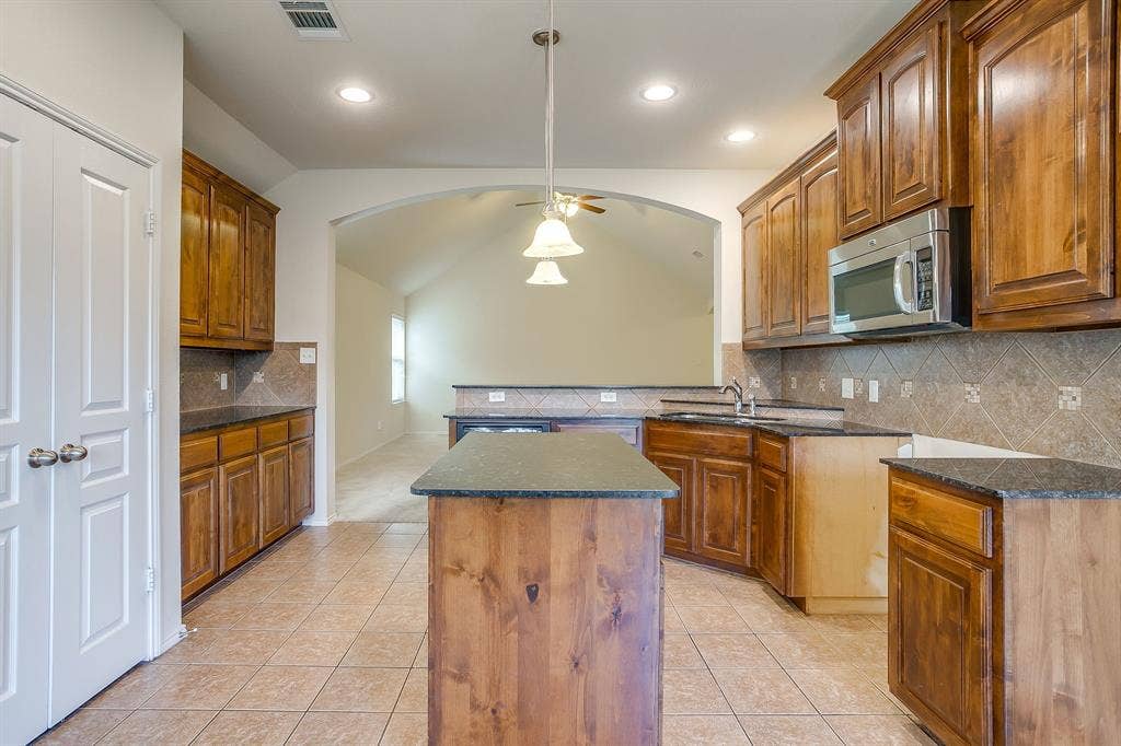 Kitchen featuring stained wood cabinetry, central island, stone-finish countertops, tile backsplash, and recessed lighting