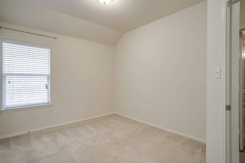 Interior room featuring neutral-toned carpeting, vaulted ceiling, and a single-pane window with horizontal blinds