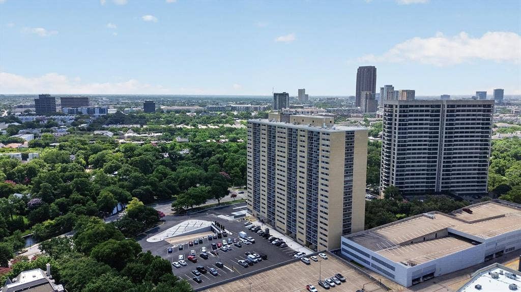 Aerial perspective of a high-rise residential complex featuring a paved surface parking lot, structured parking, and mature tree canopy