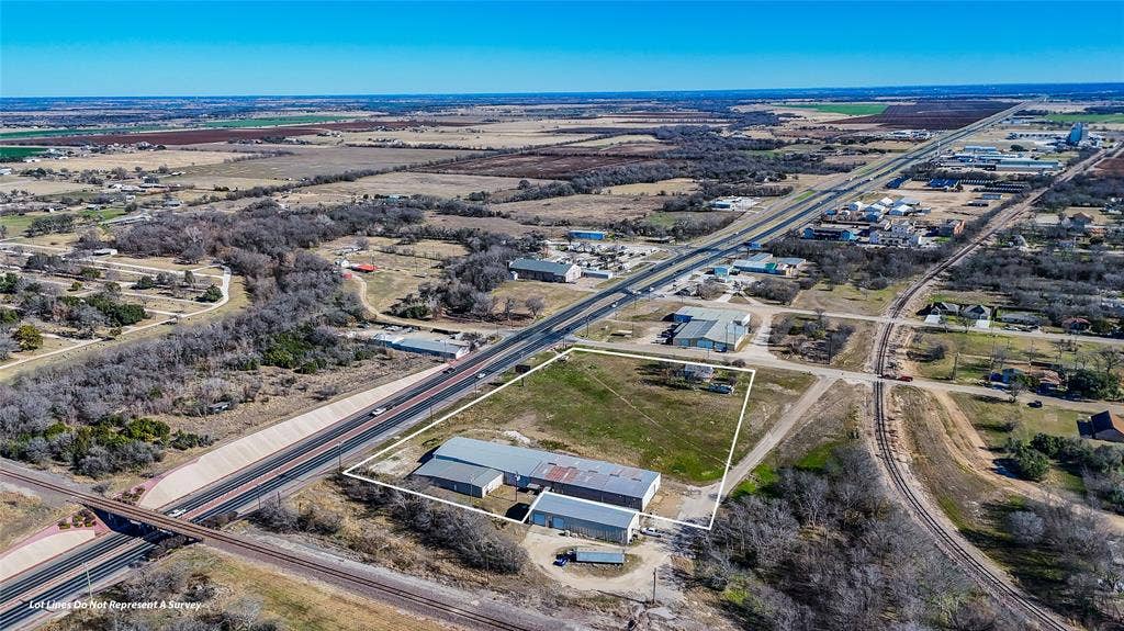 110 1st Street, McGregor, TX 76657 Aerial perspective featuring a multi-building property with expansive open land, metal-roof structures, and immediate proximity to a major thoroughfare and rail infrastructure