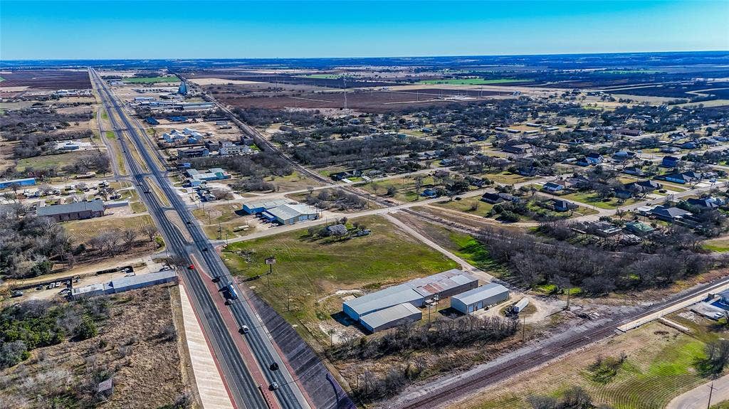 110 1st Street, McGregor, TX 76657 Aerial perspective featuring expansive acreage, industrial structures with metal roofing, direct highway frontage, and railroad line access