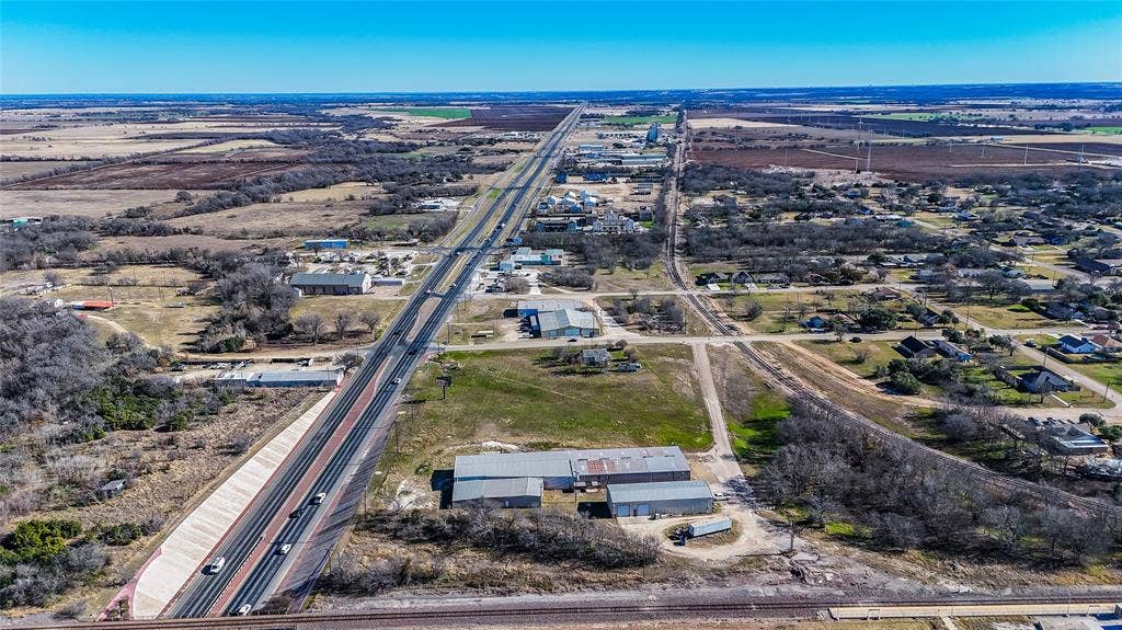 110 1st Street, McGregor, TX 76657 Aerial perspective featuring a multi-building structure with metal roofing, expansive acreage, and direct proximity to major thoroughfares and railway infrastructure