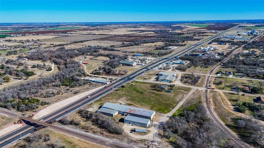 110 1st Street, McGregor, TX 76657 Aerial perspective of a multi-structure property featuring metal-roofed industrial facilities, expansive acreage, paved access points, and proximity to major regional transportation infrastructure